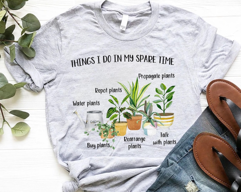 以下が含まれることがあります： 「Things I do in my spare time」というテキストと、「Propagate plants」、「Repot plants」、「Water plants」、「Buy plants」、「Rearrange plants」、「Talk with plants」などの植物関連の活動のリストが書かれたグレーのTシャツ。テキストは鉢植えの植物のイラストで囲まれています。