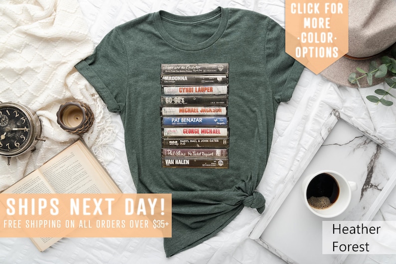 May include: A green t-shirt with a stack of vintage cassette tapes featuring artists like Madonna, Cyndi Lauper, Michael Jackson, Pat Benatar, George Michael, Van Halen, and more.