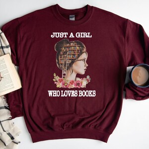 Pu&ograve; includere: Felpa color borgogna con una grafica di una donna con una libreria per la testa e il testo "Just a girl who loves books".