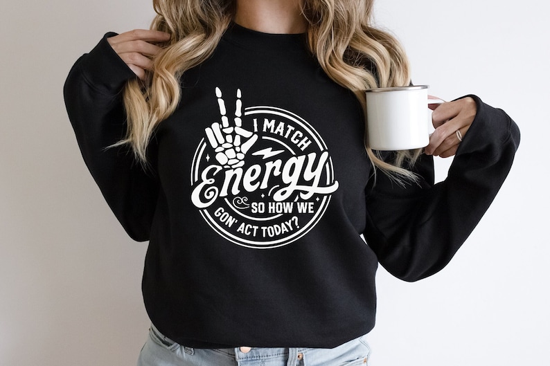 Op de afbeelding: Zwart sweatshirt met een wit grafisch ontwerp met een skelethand die een peace-teken maakt en de tekst "I Match Energy So How We Gon' Act Today?"