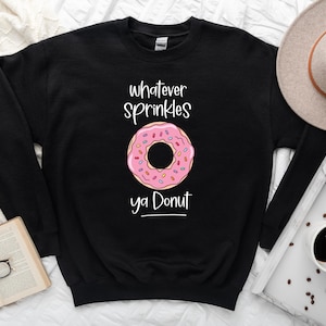 May include: Black sweatshirt with a pink and white donut graphic and the text "whatever sprinkles ya donut".