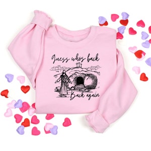 May include: Pink sweatshirt with a black and white illustration of Jesus walking out of a tomb with the text "Guess who's back back again".