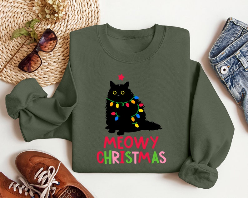 May include: A green sweatshirt with a black cat wearing Christmas lights and the text "MEOWY CHRISTMAS" in red, green, and pink.