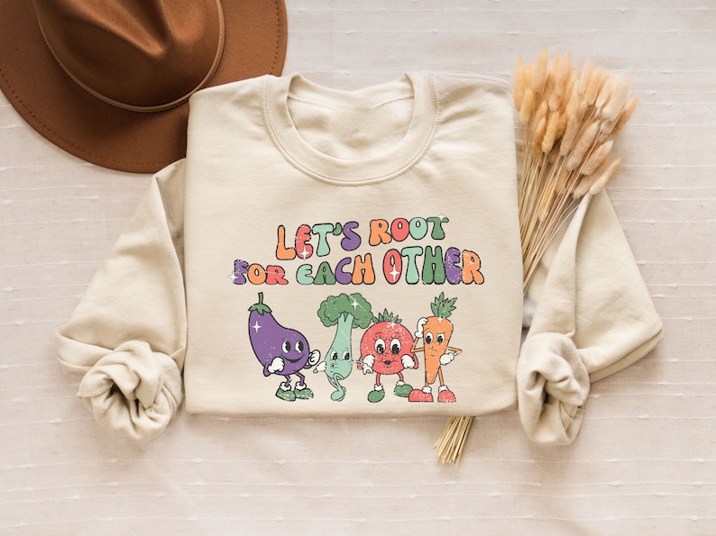 May include: A beige sweatshirt with a graphic of four cartoon vegetables and the text "Let's Root For Each Other".