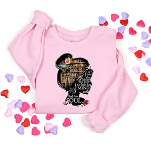 May include: Pink sweatshirt with a black silhouette of a woman reading in a library. The text reads "& into the library she goes to lose her MIND and find her SOUL."