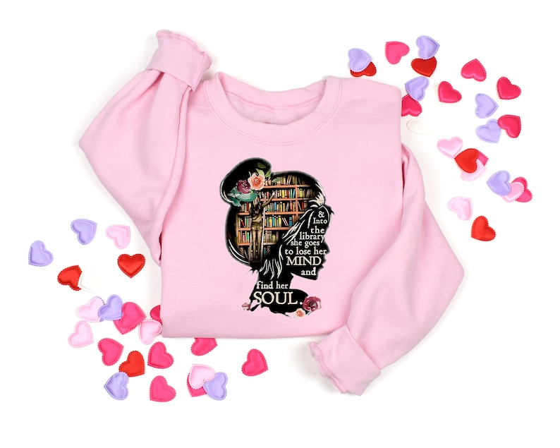 May include: Pink sweatshirt with a black silhouette of a woman reading in a library. The text reads "& into the library she goes to lose her MIND and find her SOUL."