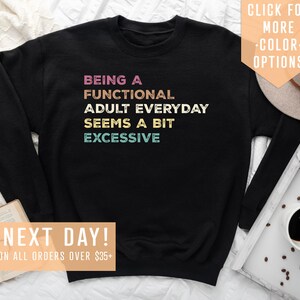 May include: Black sweatshirt with the text "BEING A FUNCTIONAL ADULT EVERYDAY SEEMS A BIT EXCESSIVE" in colorful retro lettering.