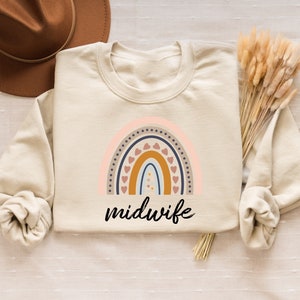 Peut inclure: Un sweat-shirt beige avec un motif arc-en-ciel et le mot "sage-femme" imprim&eacute; dessus.