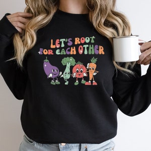 May include: Black sweatshirt with a colorful graphic of vegetables with faces and the text "Let's root for each other".