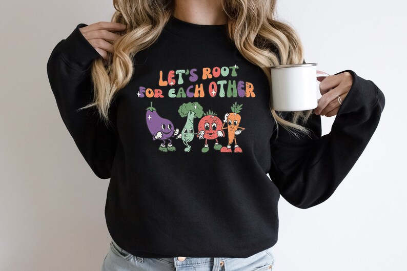 May include: Black sweatshirt with a colorful graphic of vegetables with faces and the text "Let's root for each other".