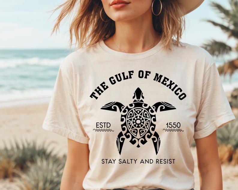 May include: Cream-colored t-shirt featuring a black turtle design with the text "THE GULF OF MEXICO" and "ESTD 1550". The shirt also includes the phrase "STAY SALTY AND RESIST".