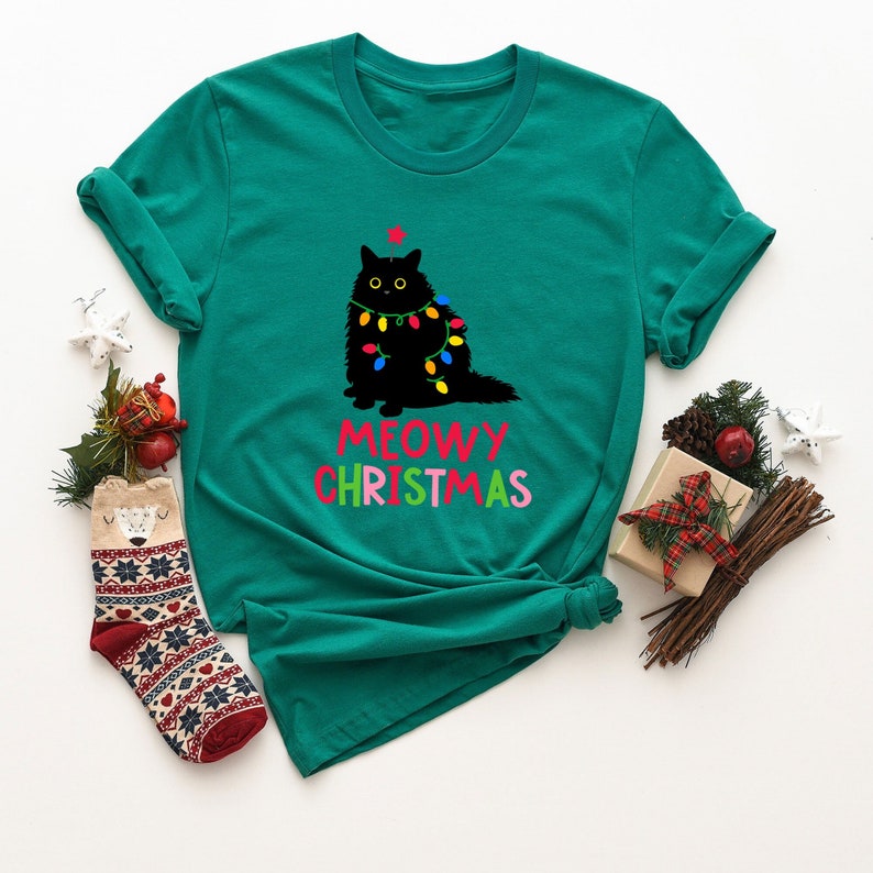 May include: A teal green t-shirt with a black cat wearing Christmas lights and the text "MEOWY CHRISTMAS" in rainbow colors.