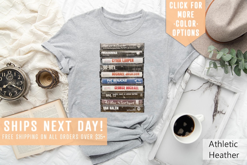 May include: A heather grey t-shirt with a graphic of a stack of vintage cassette tapes featuring artists like Madonna, Cyndi Lauper, and Van Halen. The text "SHIPS NEXT DAY! FREE SHIPPING ON ALL ORDERS OVER $35+" is at the bottom of the image.