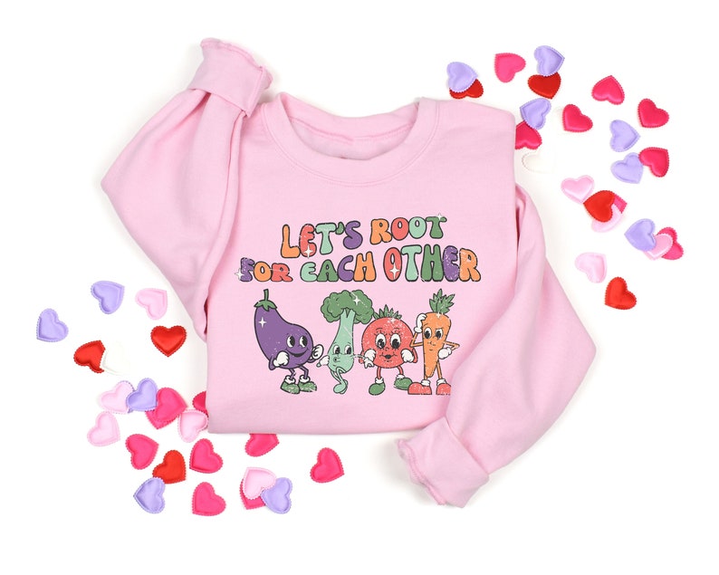 May include: Pink sweatshirt with a graphic of smiling vegetables and the text "Let's Root For Each Other".