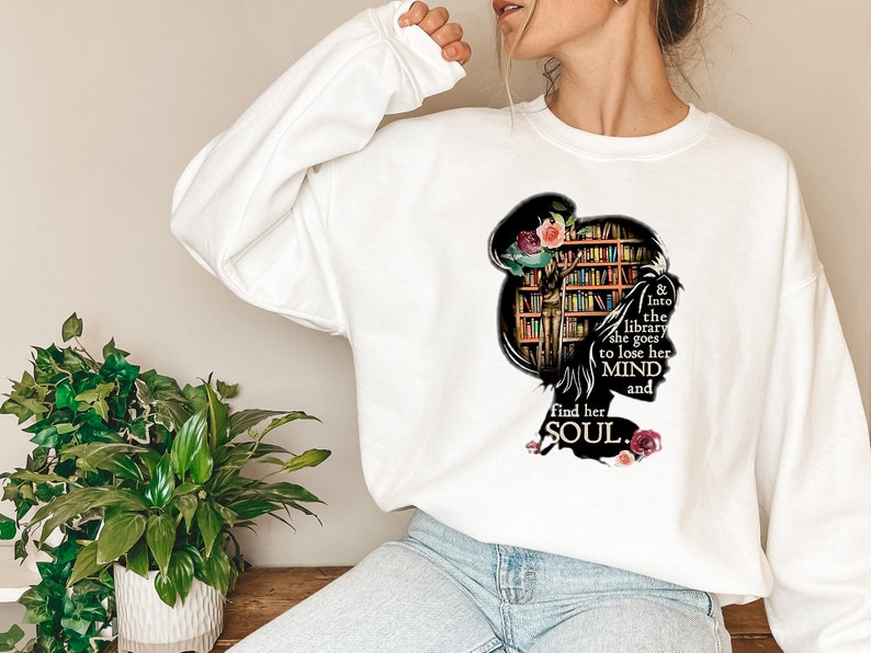 May include: White sweatshirt with a graphic of a woman's silhouette with a bookshelf for a head. The text reads "& into the library she goes to lose her MIND and find her SOUL."