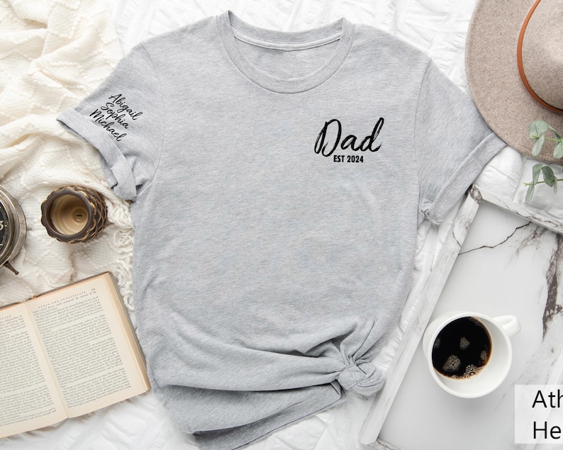 May include: Gray t-shirt with the text "Dad Est 2024" on the front and the names "Abigail, Sophia, Michael" on the sleeve.