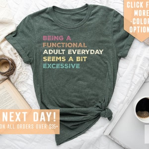 May include: Green t-shirt with the text "Being a Functional Adult Everyday Seems a Bit Excessive" in rainbow colors.