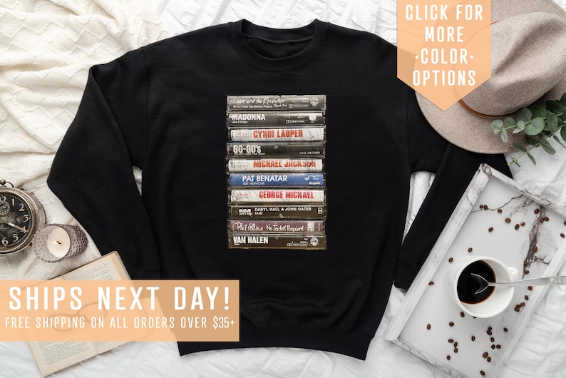 May include: Black sweatshirt with a graphic of a stack of vintage cassette tapes featuring artists like Madonna, Cyndi Lauper, Michael Jackson, Pat Benatar, George Michael, Phil Collins, and Van Halen. The text "SHIPS NEXT DAY! FREE SHIPPING ON ALL ORDERS OVER $35+" is at the bottom of the image.