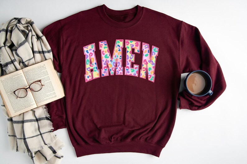 Puede incluir: Sudadera color burdeos con un gran gr&aacute;fico "AMEN" colorido en un dise&ntilde;o de estampado de leopardo.