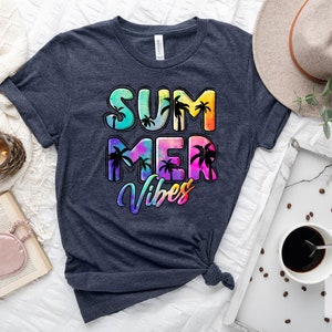 May include: Heather navy t-shirt with the words "SUMMER VIBES" in a colorful, tropical design. The design includes palm trees and a gradient of colors. A neutral-toned hat and a tray with coffee are also visible.