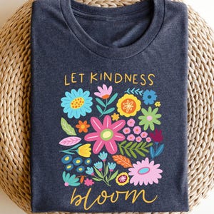 May include: A dark blue t-shirt with a colorful floral design and the text "Let Kindness Bloom".