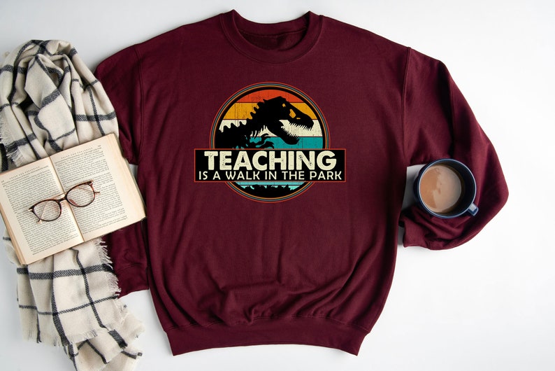 May include: Burgundy sweatshirt with a vintage-style graphic of a dinosaur with the text "Teaching is a walk in the park".