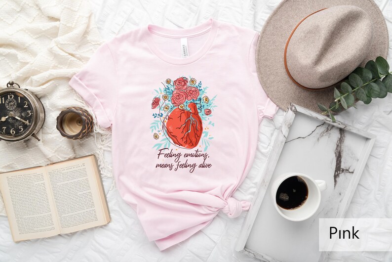 May include: Pink t-shirt featuring a graphic of a heart with flowers and the text "Feeling emotions, means feeling alive".