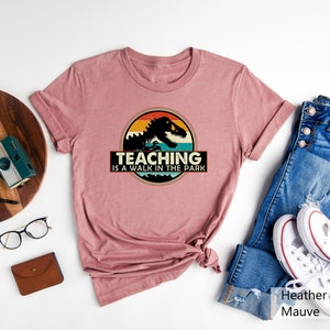 May include: A heather mauve t-shirt with a vintage-style graphic of a dinosaur with the text "Teaching is a walk in the park".