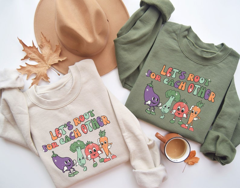 May include: Two cream and olive green sweatshirts with the text "Let's root for each other" and a graphic of cartoon vegetables.