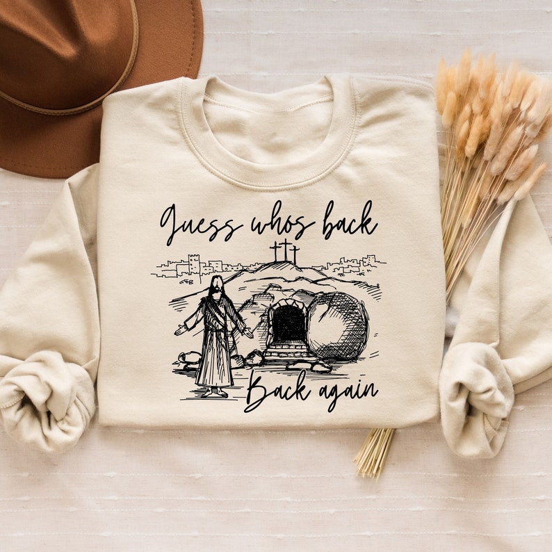 May include: A beige sweatshirt with a black graphic print of a person walking out of a tomb. The text "Guess who's back back again" is printed below the graphic.