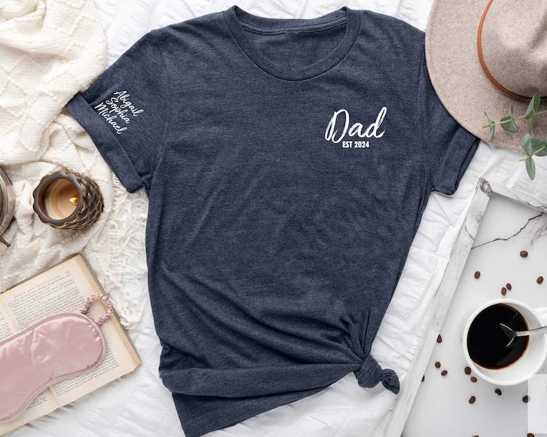 May include: A navy blue t-shirt with the text "Dad Est 2024" on the front and the names "Abigail, Sophia, Michael" on the left sleeve.