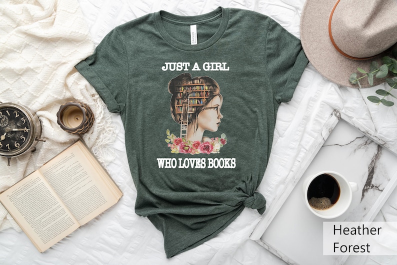 Pu&ograve; includere: Una maglietta verde con il testo "Just a girl who loves books" e un'immagine di una donna con libri impilati sulla testa.