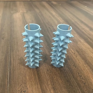 Op de afbeelding: Twee lichtblauwe plastic stuurgrepen met een stekelig ontwerp. De grepen zijn gemaakt om eruit te zien als een cactus.
