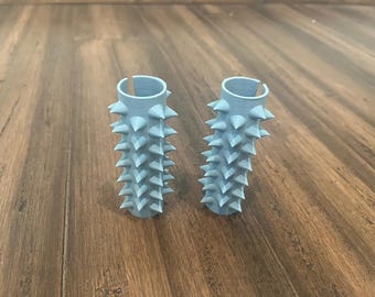 Pode incluir: Duas pegas de guiador de plástico azul claro com um design de espinhos. As pegas são feitas para parecerem um cacto.