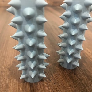 Op de afbeelding: Twee lichtblauwe, stekelige, cilindrische voorwerpen. De voorwerpen zijn gemaakt van een zacht, rubberachtig materiaal en hebben een getextureerd oppervlak. De voorwerpen zijn vergelijkbaar in grootte en vorm.