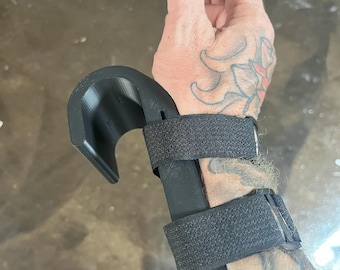 May include: Black weightlifting wrist support with hook and adjustable straps. The support is designed to wrap around the wrist and secure with hook and loop fasteners. The hook is designed to attach to a barbell or other weightlifting equipment.