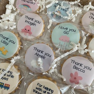 May include: A collection of round, scalloped-edge sugar biscuits individually wrapped in clear plastic. Each biscuit features a unique printed design with text such as Thank you Imogen, I love you GG, and Thank you Aimee, alongside illustrations of an octopus, cloud, sheep, and flowers.