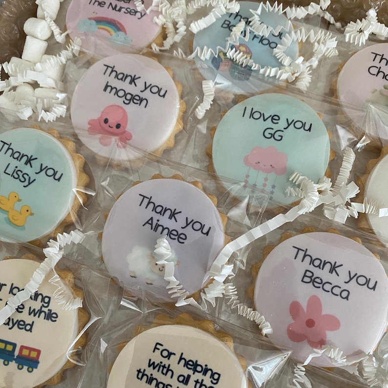 May include: A collection of round, scalloped-edge sugar biscuits individually wrapped in clear plastic. Each biscuit features a unique printed design with text such as Thank you Imogen, I love you GG, and Thank you Aimee, alongside illustrations of an octopus, cloud, sheep, and flowers.