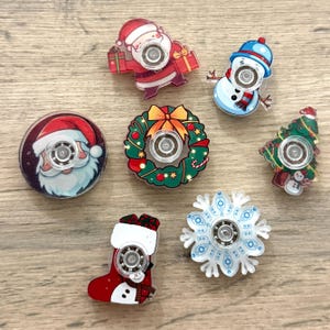 May include: A selection of Christmas-themed fidget spinners. Designs include Santa Claus, a snowman, a Christmas tree, a wreath, a stocking, and a snowflake. Each spinner has a central bearing and colourful graphics.