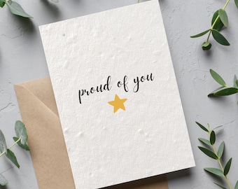 May include: A white card with the words "proud of you" written in black cursive. A small yellow star is below the text.