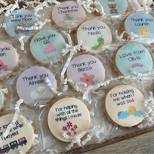 May include: A collection of round biscuits individually wrapped in clear plastic, each featuring a unique printed design with text such as Thank you Charlotte, Thank you Nadia, Love from Olivia, and For helping with all the things I made.