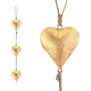 May include: Gold-coloured metal heart-shaped wind chimes hanging from natural twine. The chimes feature three smaller hearts strung together and a larger heart suspended separately. The metal has a slightly textured surface.