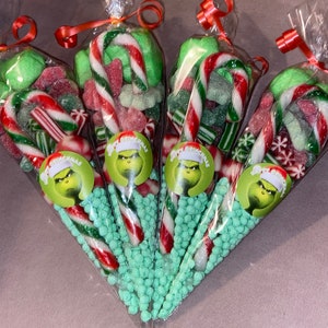 May include: Four cellophane bags filled with sweets. Each bag contains green sweets, red and white striped candy canes, green and red gummy sweets, and a Grinch sticker. Tied with red ribbon.