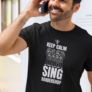 Puede incluir: Una camiseta negra con un diseño gráfico blanco que dice "Keep Calm Sing Barbershop". El gráfico presenta un cuarteto de barbería cantando.