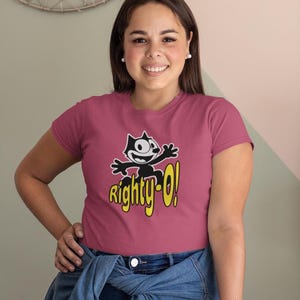 May include: A pink t-shirt with a black and white cartoon cat wearing a yellow hat and the text "Righty-O!" in yellow.