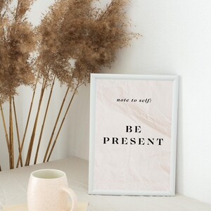 May include: A white framed print with a beige background and the text "note to self: BE PRESENT" in black lettering.