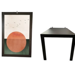 Pode incluir: Uma mesa retangular marrom escuro com pernas anguladas e uma obra de arte emoldurada. A obra de arte apresenta um design minimalista com um grande círculo laranja, uma seção verde e um fundo bege com pássaros voando.