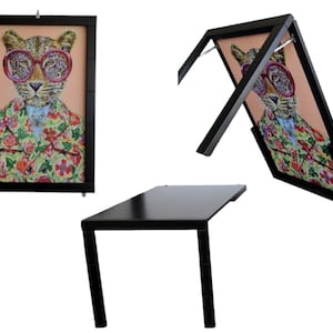 Könnte beinhalten: Ein schwarzes gerahmtes Bild eines Leoparden mit Sonnenbrille und einer Jacke mit Blumenmuster. Das Bild ist an einem schwarzen Klapptisch befestigt.