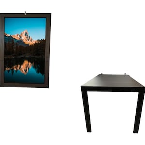 Può includere: Un'opera d'arte da parete rettangolare marrone scuro incorniciata con una scena di paesaggio montano con un lago. Accanto, un tavolo rettangolare marrone scuro con quattro gambe.