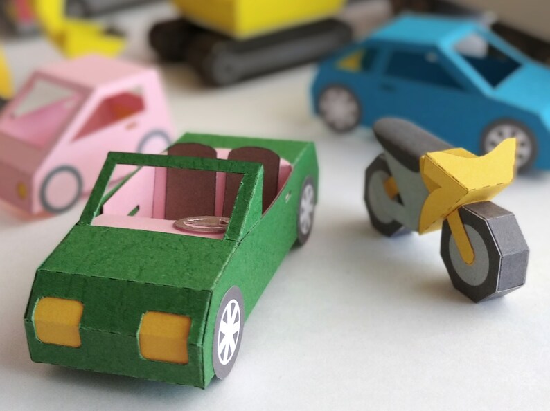 May include: A collection of colorful paper toy vehicles, including a green convertible, a pink car, a blue sedan, a yellow motorcycle, and a yellow construction vehicle. The vehicles are made of folded paper and have detailed features.